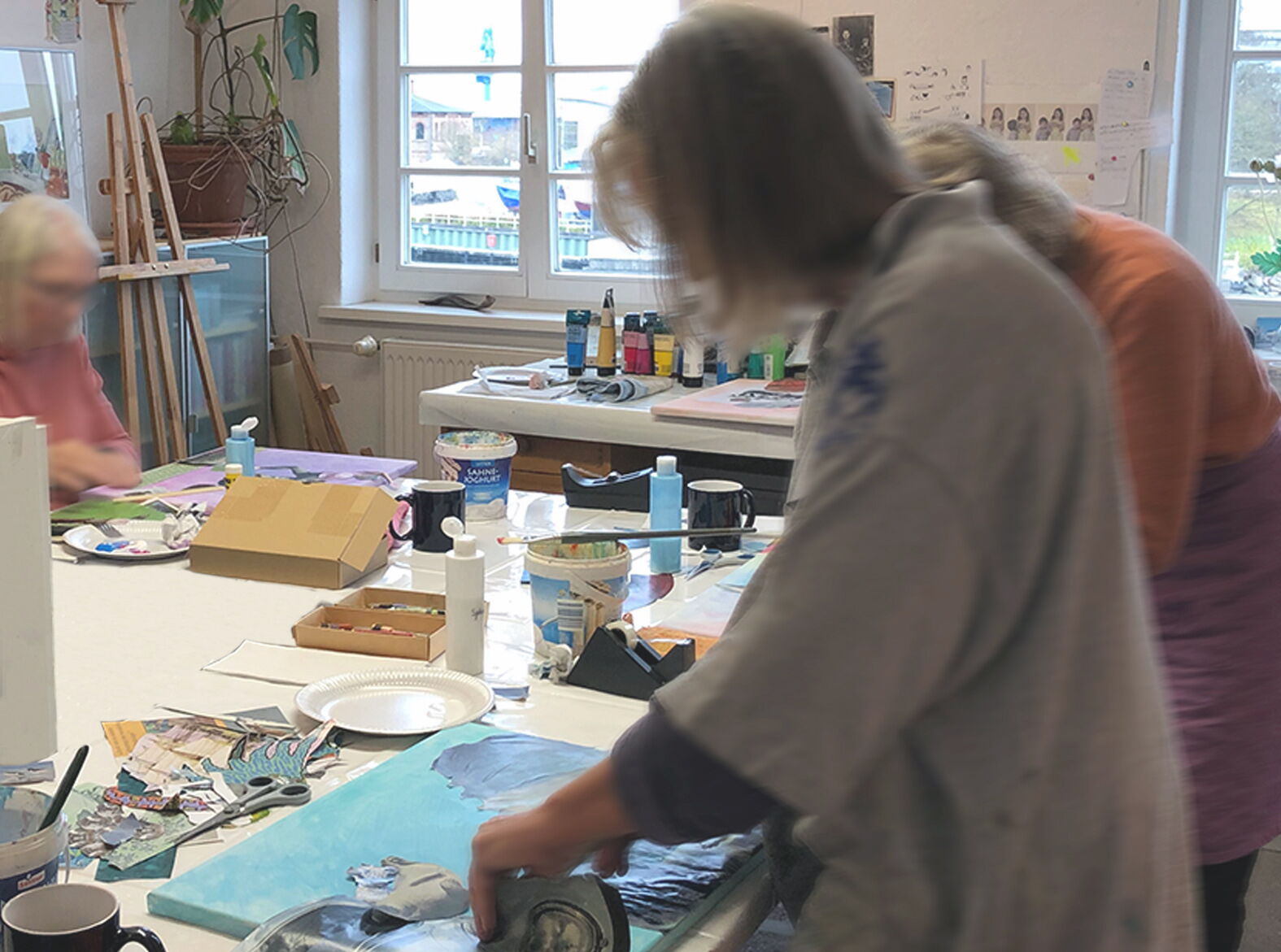 Drei Künstlerinnen arbeiten konzentriert an ihren Bildern während des Collage-Workshops in dem kreativen Kunst Atelier der Malerin und Illustratorin Edda Skibbe.